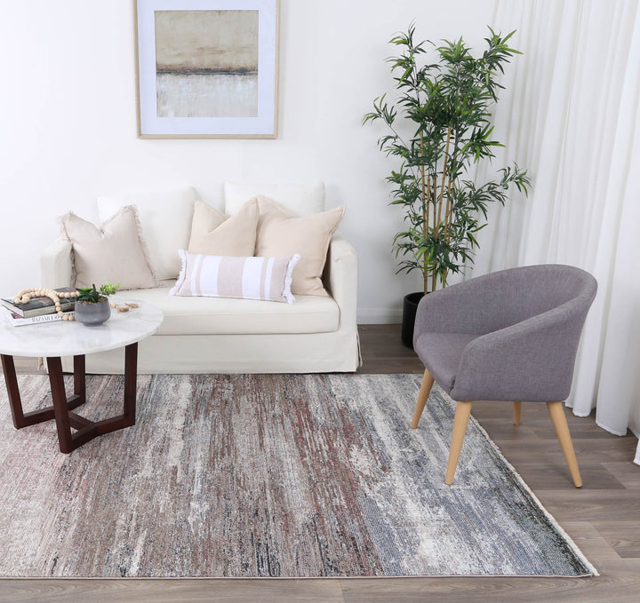Modern living room with beige sofa, accent pillows, gray armchair, abstract rug, and indoor plant