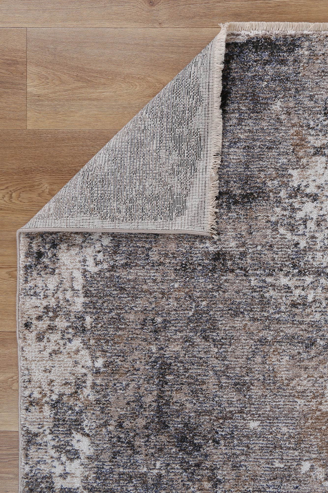 Modern area rug with distressed pattern in beige and brown on hardwood floor