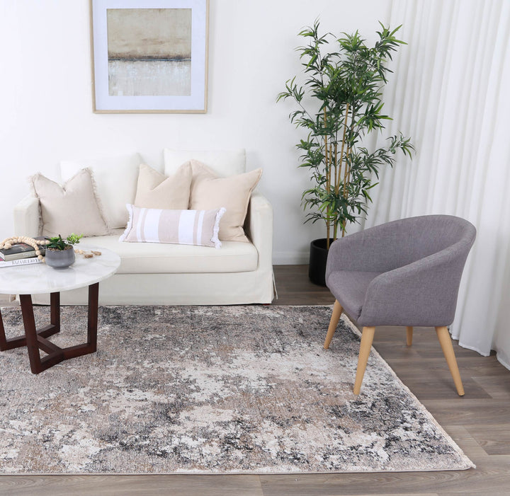 Modern living room with white sofa, gray armchair, abstract rug, coffee table, and potted plant