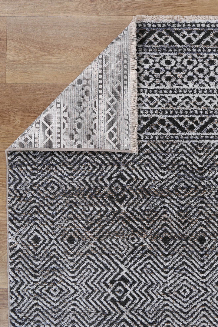 Black and white geometric patterned area rug with corner flipped on wood floor