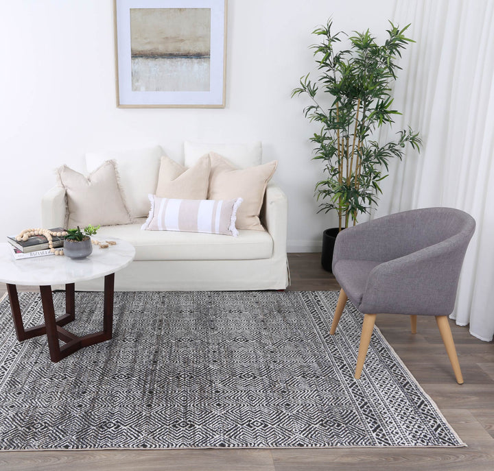 Modern living room with white sofa, neutral pillows, accent chair, patterned rug, and indoor plant