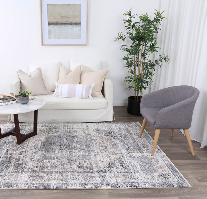 Modern living room with a white sofa, decorative pillows, gray accent chair, indoor plant, abstract wall art, coffee table, and patterned area rug.