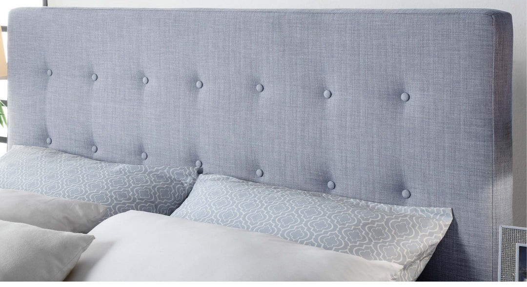 Light grey upholstered bed headboard with button tufting and patterned pillows