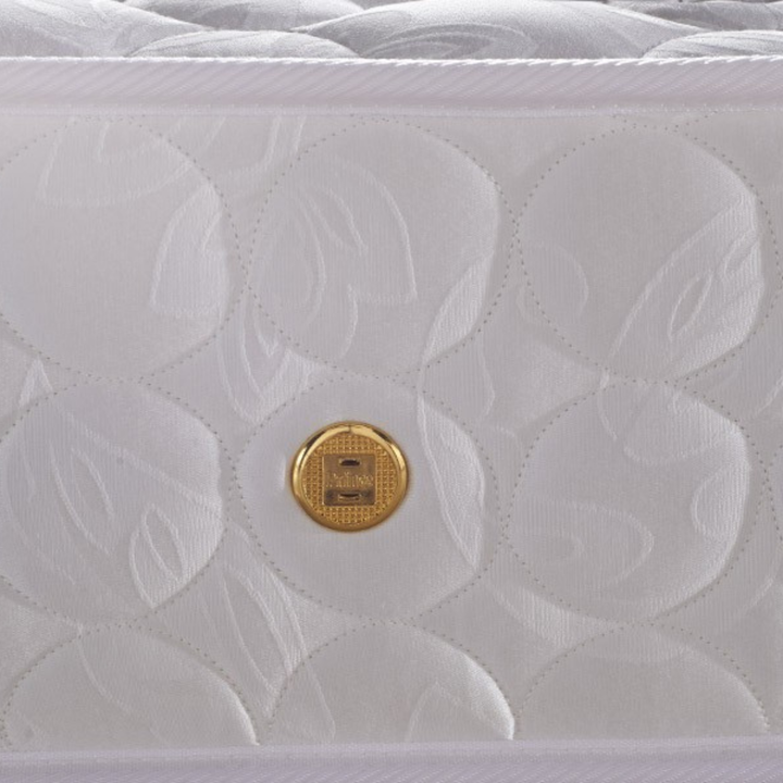 Close-up of white quilted luxury mattress with gold emblem, textured fabric design