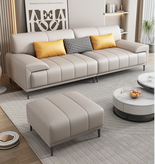 Modern beige leather sofa with yellow and patterned pillows, matching ottoman, and round coffee table in stylish living room
