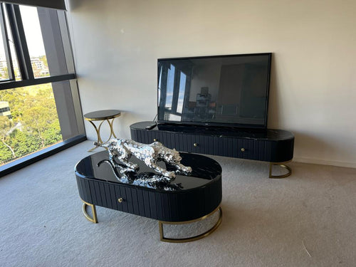 Black gloss TV unit and matching oval coffee table with gold legs, featuring a silver leopard sculpture in modern living room