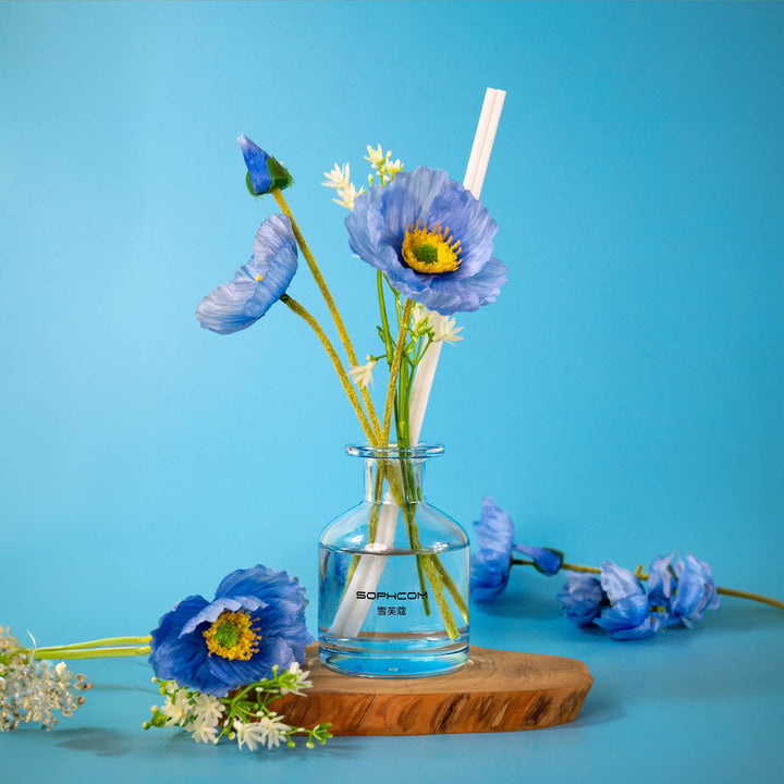 Blue poppy flowers in a glass vase on wooden tray, minimalist home decor on blue background.