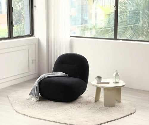 Modern black lounge chair with throw blanket, round coffee table, and decor in bright living room