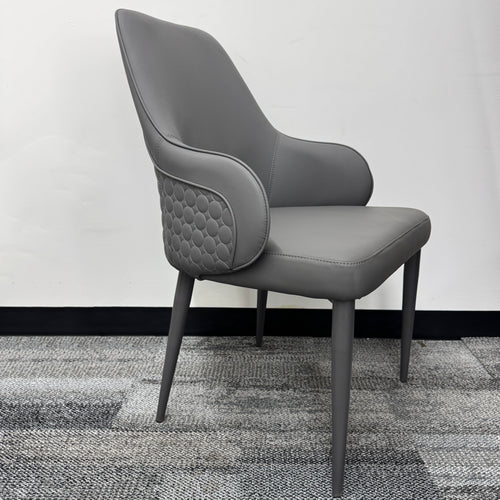 Modern grey upholstered armchair with quilted sides, minimalist design, on carpeted floor