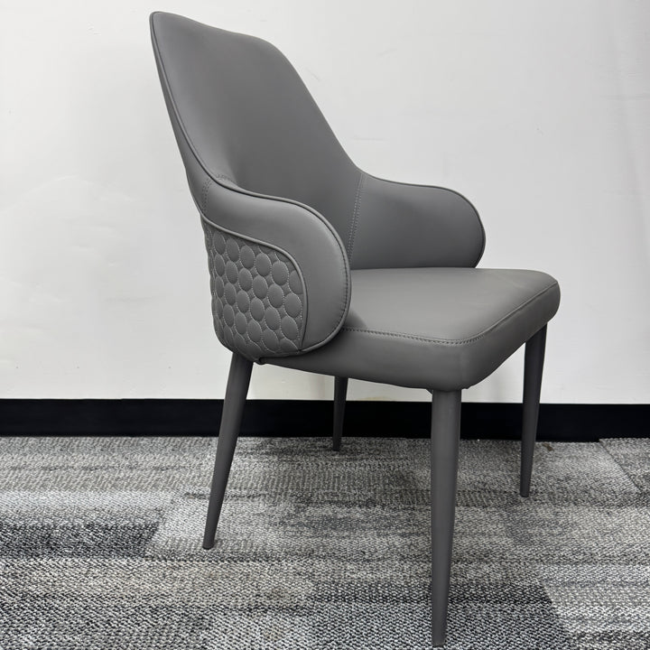 Modern grey upholstered armchair with quilted sides, minimalist design, on carpeted floor