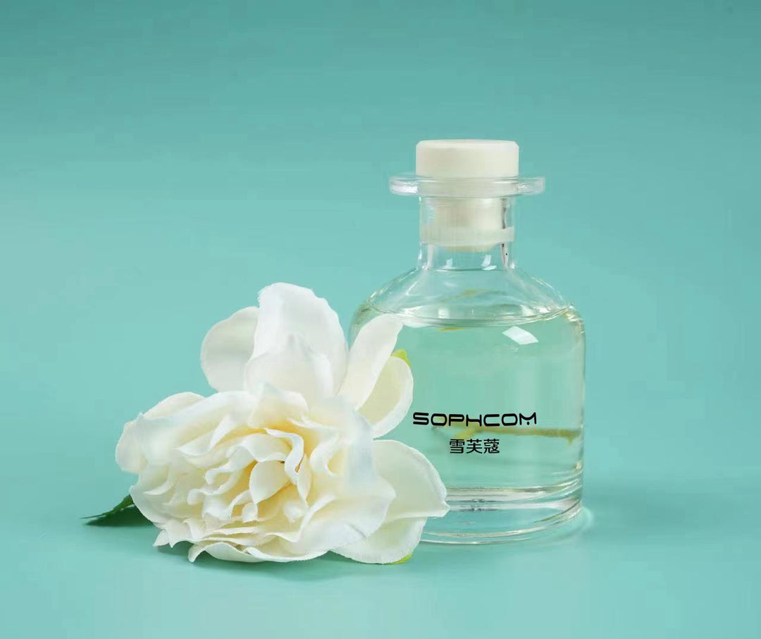 Clear glass perfume bottle with white flower and aqua background