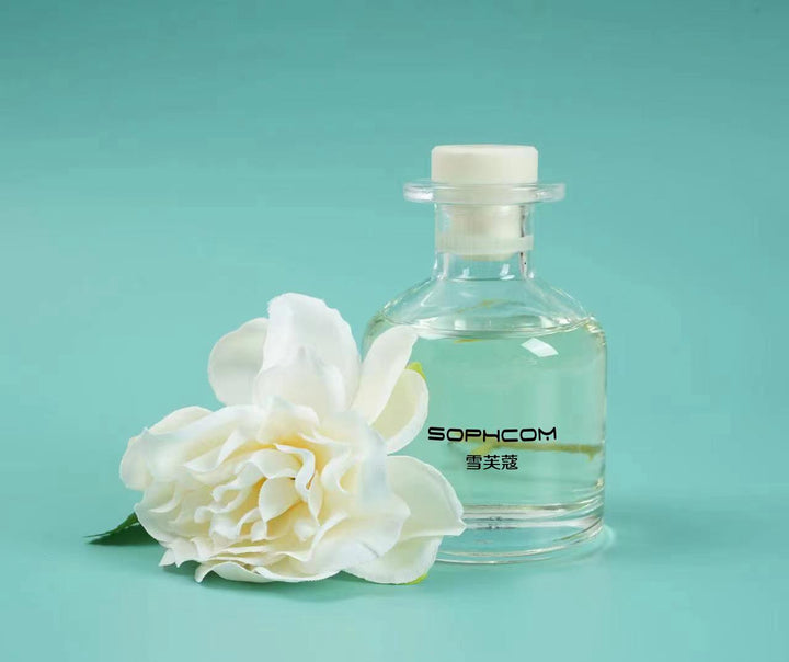 Clear glass perfume bottle with white flower and aqua background