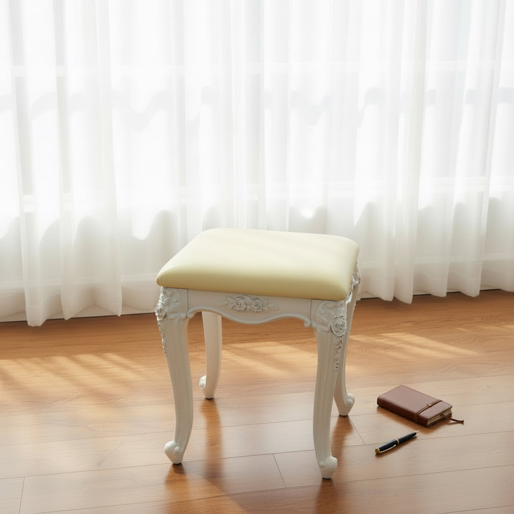 Elegant white vanity stool with cushioned seat on wood floor near notebook and pen, bright room