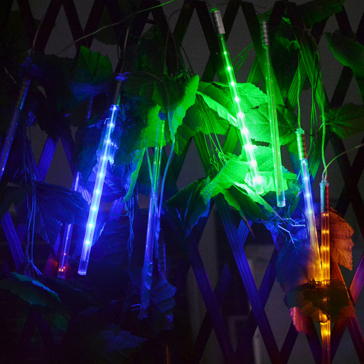 Solar LED meteor shower lights in blue, green, and yellow on outdoor foliage at night